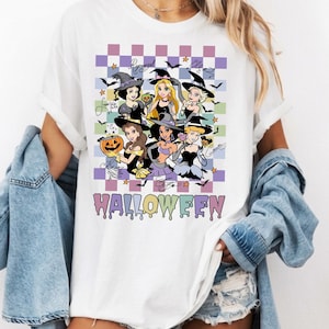 May include: A white t-shirt featuring a graphic print of six animated characters dressed as witches, set against a purple and white checkered background with bats and stars. The word HALLOWEEN is printed in a dripping, colorful font below.