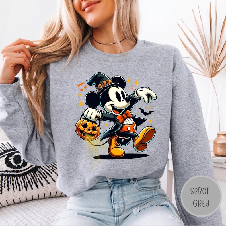 May include: A heather gray sweatshirt featuring a graphic of Mickey Mouse dressed as a wizard with a pumpkin bucket, an orange bow tie, and a hat with skull accents. The design includes small orange stars, musical notes, and a black bat silhouette.