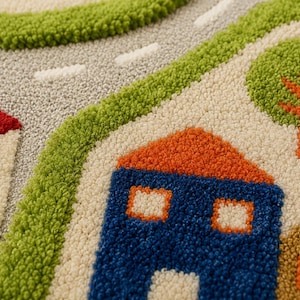 May include: A tufted rug featuring a colorful town scene with a gray road, green grass, and houses with red, orange, and blue roofs. The textured surface displays detailed patterns of trees and buildings in vibrant shades of red, blue, and green.