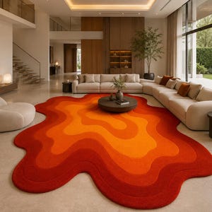May include: An irregular, organic-shaped area rug featuring a layered, wavy pattern in vibrant shades of red, orange, and yellow. The rug has a soft, textured surface and is positioned on a light-coloured floor in a large, open-concept living space.