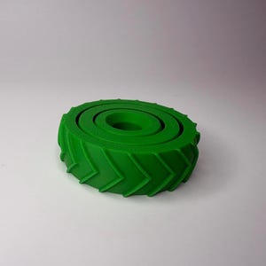 May include: A bright green, 3D-printed object resembling a tire. The tire has a circular shape with a central hole and concentric rings. The outer edge features a chevron pattern. The object is likely a decorative item or a component for a larger project.