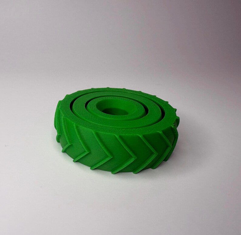 May include: A bright green, 3D-printed object resembling a tire. The tire has a circular shape with a central hole and concentric rings. The outer edge features a chevron pattern. The object is likely a decorative item or a component for a larger project.