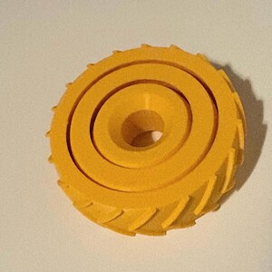 May include: A bright yellow, circular object with a spiral design and a central hole. The outer edge features a series of small, angled ridges. The object appears to be made of a solid material.