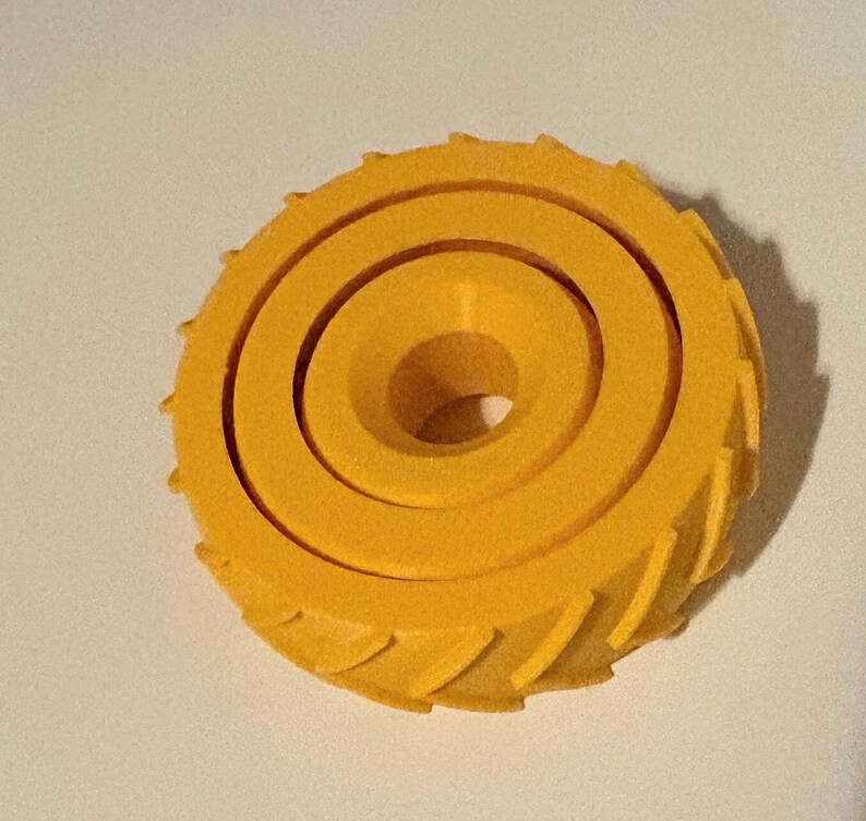 May include: A bright yellow, circular object with a spiral design and a central hole. The outer edge features a series of small, angled ridges. The object appears to be made of a solid material.