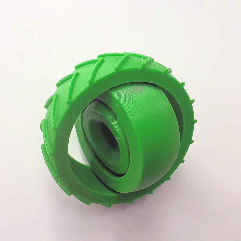 May include: A bright green, 3D-printed toy featuring a wheel-like design. The outer ring has a textured tread pattern, and the inner section is a solid, rounded shape. The toy is made of a smooth, solid material and is set against a white background.
