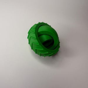 May include: A bright green, 3D-printed toy resembling a tire. The toy has a ridged outer edge and a smooth, curved inner section. The object is designed to roll and is likely a children's toy.