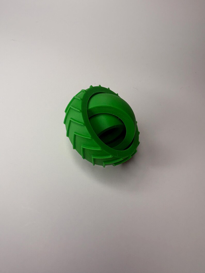 May include: A bright green, 3D-printed toy resembling a tire. The toy has a ridged outer edge and a smooth, curved inner section. The object is designed to roll and is likely a children's toy.