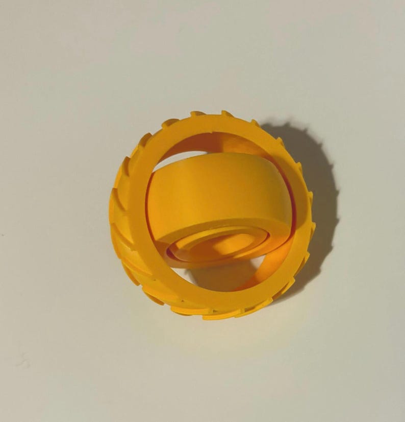 May include: A bright yellow, 3D-printed fidget toy. The toy features a circular outer ring with ridged edges and an inner, cylindrical component. The design allows for spinning and tactile interaction, promoting focus and stress relief.