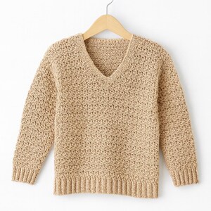 Puede incluir: Un suéter beige con cuello en V y mangas largas, exhibido en una percha de madera. El suéter tiene una apariencia tejida texturizada y puños y dobladillo acanalados. La prenda está hecha de un material suave y cálido.