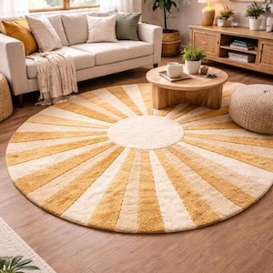 May include: A large circular area rug featuring a sunburst pattern with alternating rays of mustard yellow and cream white. The rug has a textured, tufted pile surface and is positioned on a wooden floor in front of a sofa and coffee table.