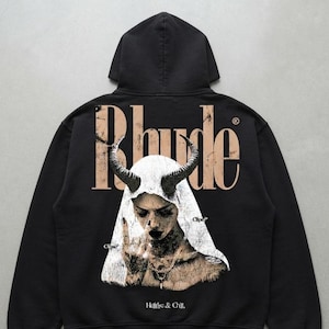 May include: A black hooded sweatshirt featuring a large graphic on the back. The design includes the text Rhude in a distressed tan font above an illustration of a figure with horns wearing a veil, with the text Hellfire & Chill at the bottom.