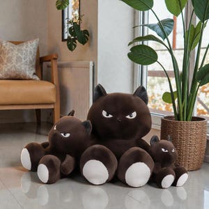 May include: A collection of brown plush cat toys with white paws and angry eyes. The toys vary in size, with the largest one in the center. The toys are arranged in front of a window with a potted plant.