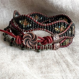 May include: A multi-layered bracelet with black, brown, and green beads, leather cord, and a copper flower charm.
