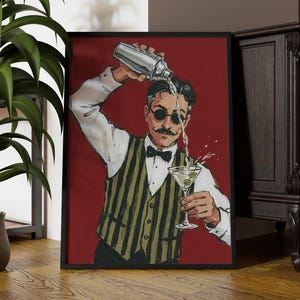 May include: A framed art print featuring a stylised illustration of a bartender with a moustache and round sunglasses, wearing a white shirt and a striped waistcoat, pouring a drink from a silver shaker into a martini glass against a deep red background.
