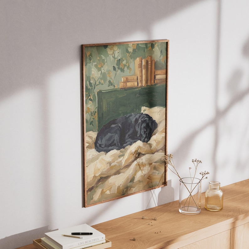 A framed print of the sleeping black Lab painting hanging on a warm beige wall above a cozy wooden console table with autumn decor.
