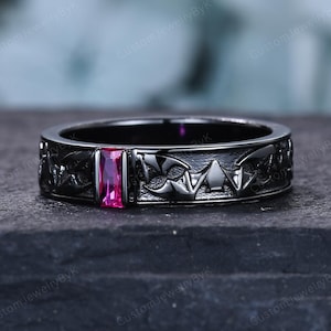 May include: A black metal band ring featuring a repeating embossed bat wing pattern around the circumference and a single rectangular baguette-cut vibrant pink gemstone set securely in the center of the band's front-facing surface.