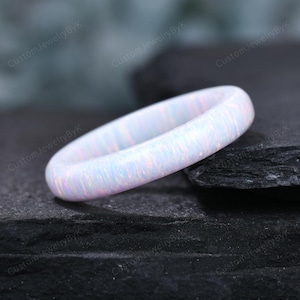 May include: A white opal ring with a smooth, polished surface. The ring has a band design and displays iridescent colors. The ring is a piece of jewelry.