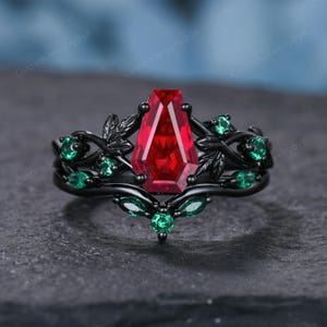Può includere: Un anello nero con una grande gemma rossa rettangolare come elemento centrale. L'anello è adornato con gemme verdi e dettagli a forma di foglia. L'anello ha un'estetica scura e gotica.