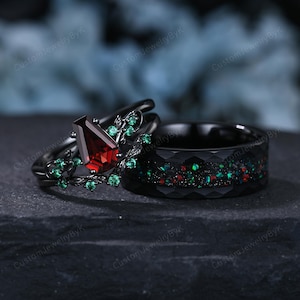 May include: A black wedding ring set. One ring features a rectangular, deep red gemstone and green accents. The other ring has a black faceted band with red and green flecks. The rings are set against a dark background.