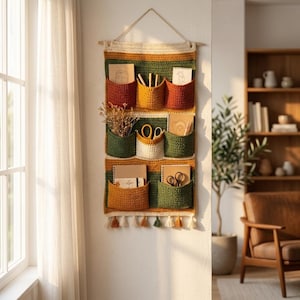 Pode incluir: Um organizador de parede em crochê com três filas horizontais de bolsos em tons de amarelo mostarda, verde floresta, creme e laranja queimado. A peça têxtil retangular está suspensa por uma haste de madeira e finalizada com borlas.