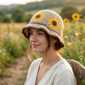 May include: A beige crochet bucket hat featuring sunflower motifs in yellow and brown. The hat has a brown brim. The hat is worn outdoors. The hat is a handmade item.