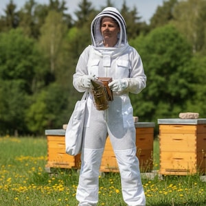May include: A beekeeper in a white protective suit and hood stands in a field of yellow flowers. They hold a smoker and a bag, with several wooden beehives in the background. The scene is set outdoors on a sunny day.
