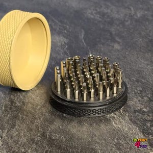 May include: A set of silver screwdriver bits arranged in a circular pattern, with a black and silver base. A light yellow, textured container is open beside the bits. The image is taken from a slightly elevated angle.