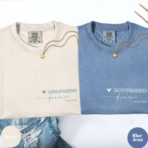 May include: Two Comfort Colors t-shirts, one ivory and one blue jean, with matching gold star necklaces. The ivory shirt says "Girlfriend" and the blue jean shirt says "Boyfriend", both with a date. The shirts are XL-TG-EG.