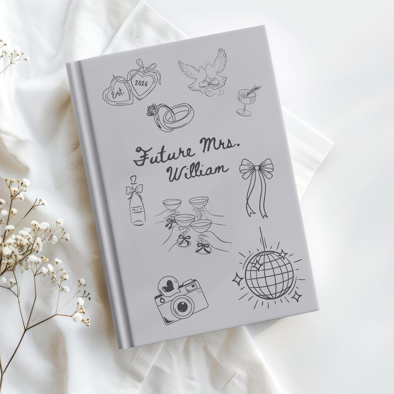 Op de afbeelding: Een grijze hardcover journal met zwarte lijntekeningen van huwelijksgerelateerde iconen, waaronder ringen, champagneglazen en een discobal. De tekst "Future Mrs. William" is in sierlijke letters geschreven.