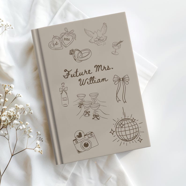 Op de afbeelding: Een lichtgrijs notitieboek met de tekst "Future Mrs. William" en diverse huwelijksthema-illustraties. De cover toont een hart, ringen, een duif, champagne, glazen, een strik, een camera en een discobal.