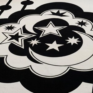 May include: A black and white patterned rug with a celestial theme. The rug features a cloud shape with stars and a crescent moon in the centre. The design is repeated across the rug.
