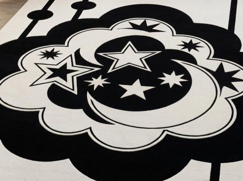 May include: A black and white patterned rug with a celestial theme. The rug features a cloud shape with stars and a crescent moon in the centre. The design is repeated across the rug.