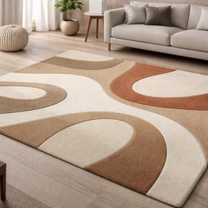 Puede incluir: Una alfombra rectangular con un diseño abstracto en tonos beige, marrón y crema. La alfombra está colocada sobre un suelo de madera. El diseño tiene un patrón curvo y fluido. También se ve un sofá y otros muebles.