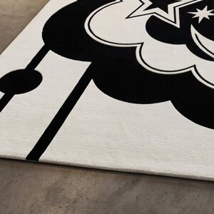May include: A monochrome rug with a celestial theme. The rug has a large cloud-like shape in black, with stars and a crescent moon. Black lines and shapes are set against a white background.