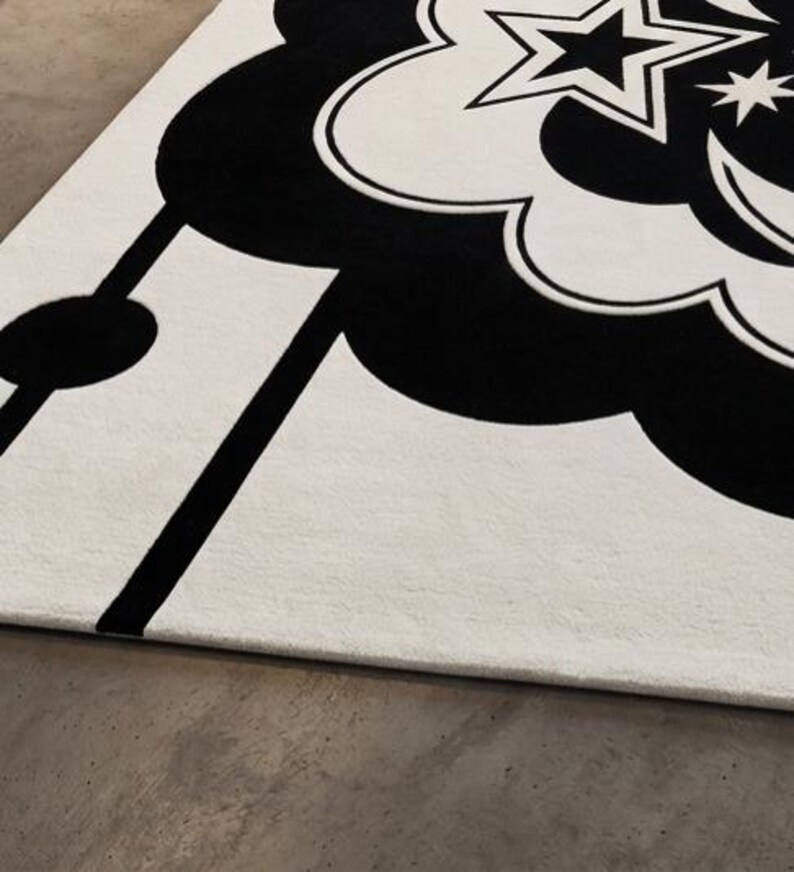 May include: A monochrome rug with a celestial theme. The rug has a large cloud-like shape in black, with stars and a crescent moon. Black lines and shapes are set against a white background.