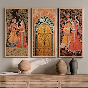 May include: Set of three framed art prints featuring Indian miniature paintings. The artwork depicts couples in traditional attire, a decorative archway, and floral backgrounds. The frames are a light wood color, and the overall color palette includes reds, yellows, and blacks.