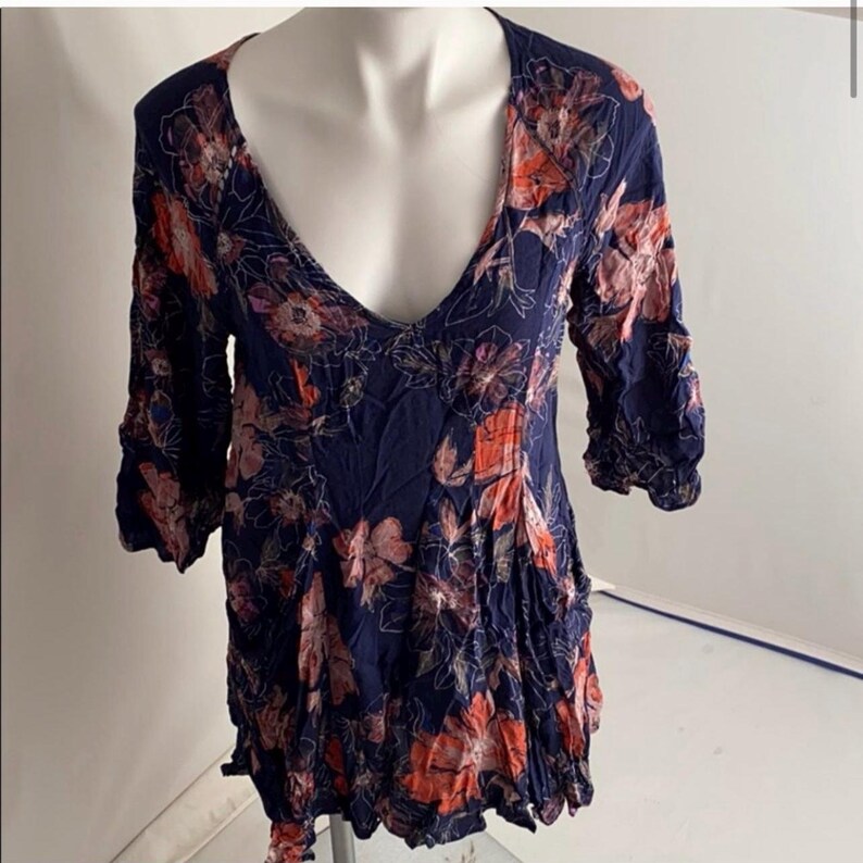 K&ouml;nnte beinhalten: Marineblaues Oberteil mit tiefem V-Ausschnitt und Dreiviertel&auml;rmeln. Das Oberteil ist mit einem Blumenmuster in Orange-, Rosa- und Wei&szlig;t&ouml;nen verziert. Der Stoff wirkt leicht und flie&szlig;end, mit leicht strukturierter Optik.