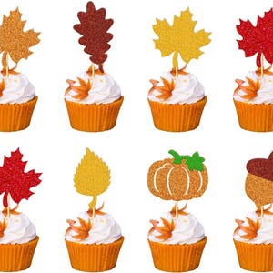 Puede incluir: Un conjunto de ocho cupcakes, cada uno coronado con un recorte de papel brillante con temática otoñal sobre un palillo de madera. Los diseños incluyen varias hojas de arce, una hoja de roble, una calabaza y una bellota en tonos rojo, naranja, amarillo y marrón.