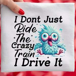 May include: White square fabric with the text "I Don't Just Ride The Crazy Train I Drive It" and a cartoon owl with wide eyes and a long tongue. The owl is teal and blue.