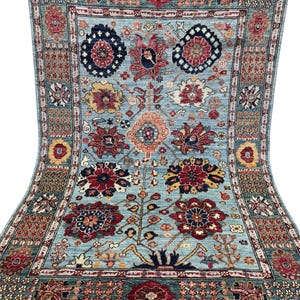 Könnte beinhalten: Ein rechteckiger, handgeknüpfter Teppich mit hellblauem Feld und aufwendigen Blumenmustern in Rot, Marine, Gelb und Pfirsich. Der Teppich hat einen detaillierten Rand und Fransen an den Kanten und zeigt ein traditionelles Design.