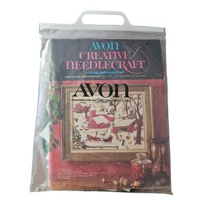 Op de afbeelding: Een Avon Creative Needlecraft crewel borduurpakket in een doorzichtige plastic tas met handvat. De verpakking bevat de tekst Winter in the Country Picture, 36 cm bij 46 cm, en vermeldt de inhoud waaronder 100 procent katoen en wol.