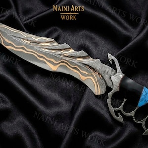 May include: A fixed-blade knife featuring a patterned Damascus steel blade with copper accents, a textured spine, and a knuckle-duster handle. The handle is black with a blue stone inlay. The text NAINI ARTS WORK is visible at the top center.