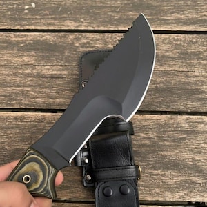 May include: A black survival knife with a partially serrated blade and a wooden handle with a black leather sheath. The knife is designed for outdoor use and survival situations.