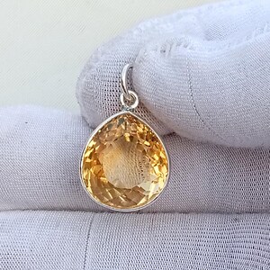 May include: A teardrop-shaped citrine pendant with a silver setting. The gemstone is a warm, golden-yellow color and has a faceted surface. The pendant is suspended from a small silver loop.