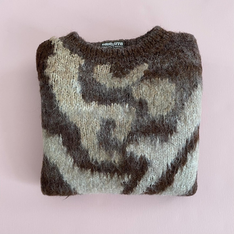 Pu&ograve; includere: Un maglione piegato con fantasia marrone, beige e grigia. Il maglione ha uno scollo tondo e un'etichetta con la scritta "vane-sita". Il maglione &egrave; realizzato in un materiale spesso e strutturato ed &egrave; piegato con cura.