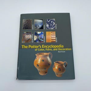 May include: A softcover book titled The Potter's Encyclopedia of Color, Form, and Decoration by Neal French. The dark gray cover features a grid of six small images showing pottery techniques and two large images of brown ceramic pitchers.
