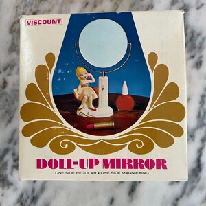 May include: A vintage "Doll-Up Mirror" box with a blue and gold design. The box features a mirror illustration, a figurine, and a lipstick. The text "VISCOUNT" is at the top, and "ONE SIDE REGULAR &bull; ONE SIDE MAGNIFYING" is at the bottom.