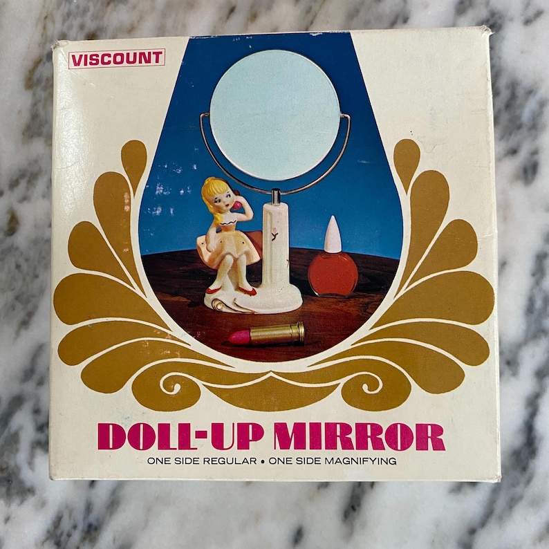 May include: A vintage "Doll-Up Mirror" box with a blue and gold design. The box features a mirror illustration, a figurine, and a lipstick. The text "VISCOUNT" is at the top, and "ONE SIDE REGULAR &bull; ONE SIDE MAGNIFYING" is at the bottom.