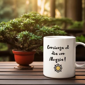 May include: White ceramic mug with the Spanish text "Comienza el dia con Alegria!" and a sun graphic. The mug is on a wooden table next to a small bonsai tree in a red pot.