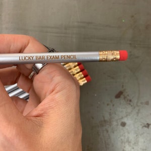 May include: A silver pencil with a red eraser and the text "LUCKY BAR EXAM PENCIL" engraved in gold.